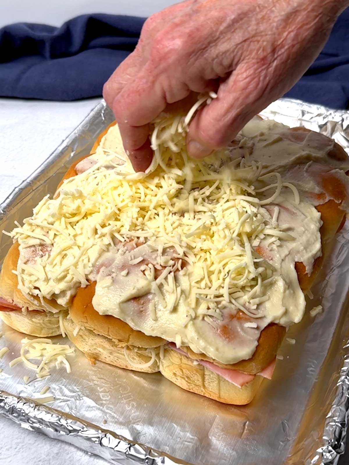Adding shredded Gruyère cheese to the top of the sliders.