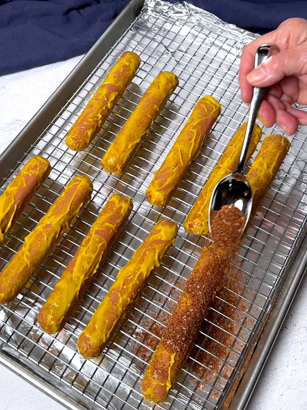 Sprinkling dry rub on the coated hot dogs.
