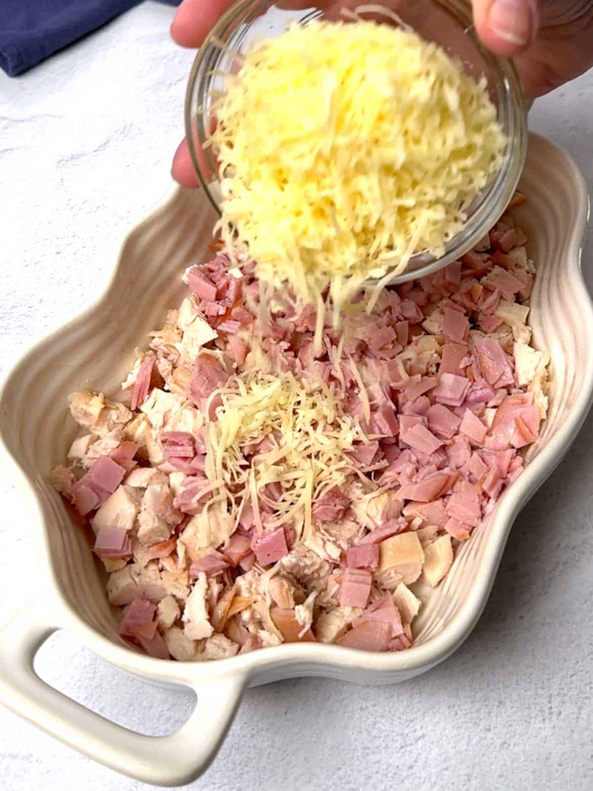Adding Gruyère cheese on top of chicken and ham.