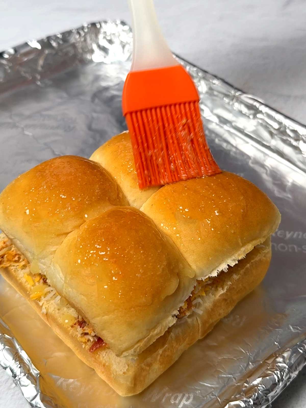 Brushing the top of the sliders with melted butter and garlic powder before baking.