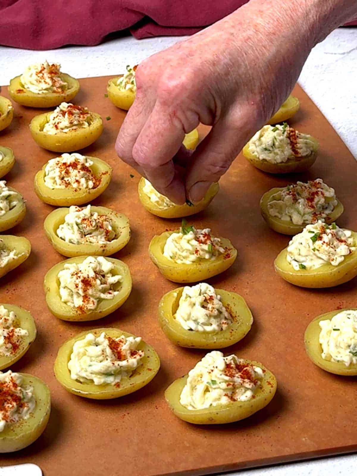 Sprinkling the deviled potatoes with minced chives.
