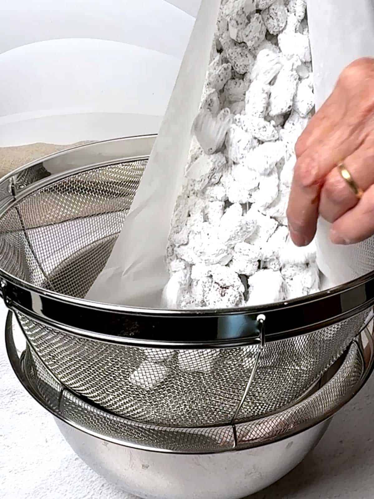 Transferring Puppy Chow to a colander to remove excess powdered sugar.