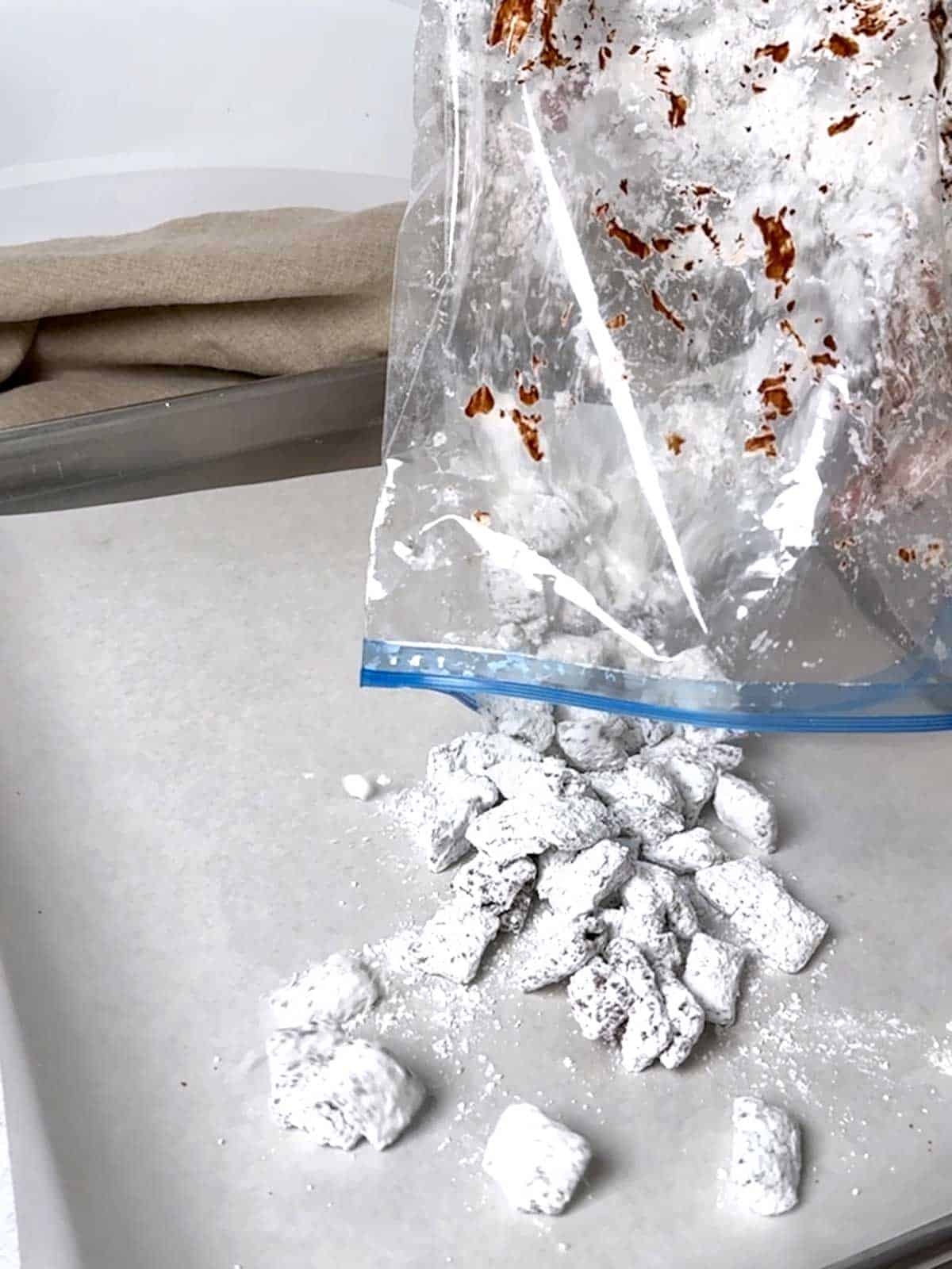 Adding the Puppy Chow to a parchment lined baking sheet to allow it to cool completely.
