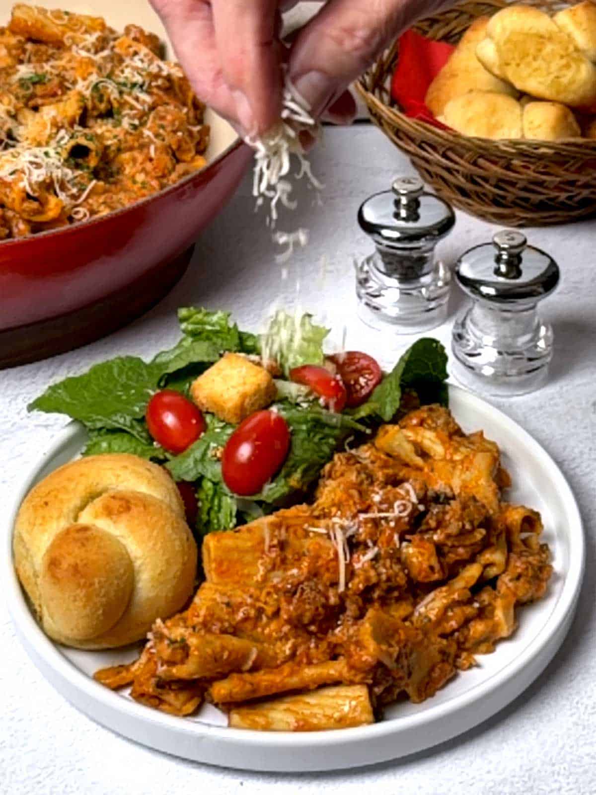 Sprinkling Parmesan cheese on the pasta.