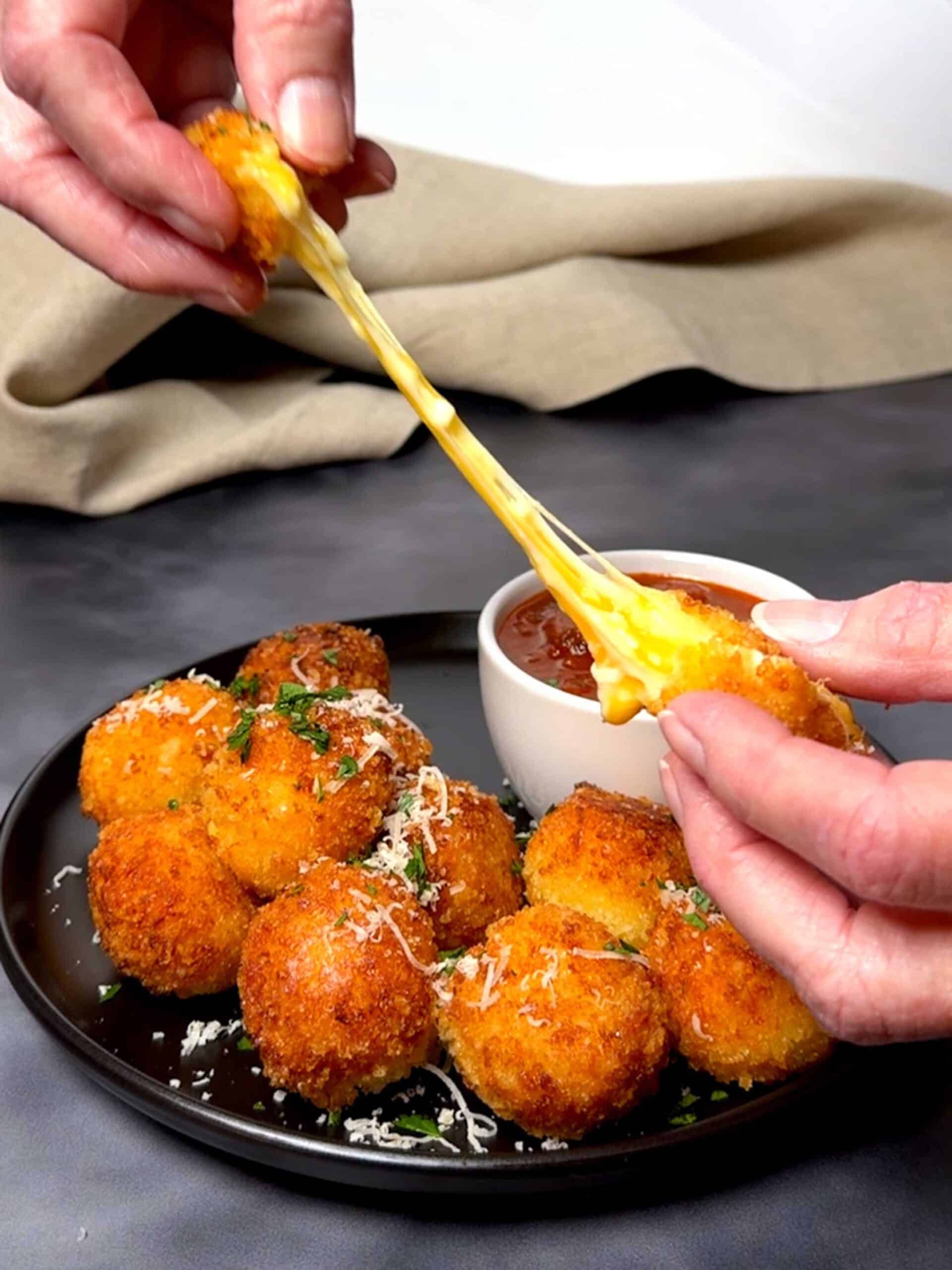 Breaking a fried cheese ball and pulling the cheese.