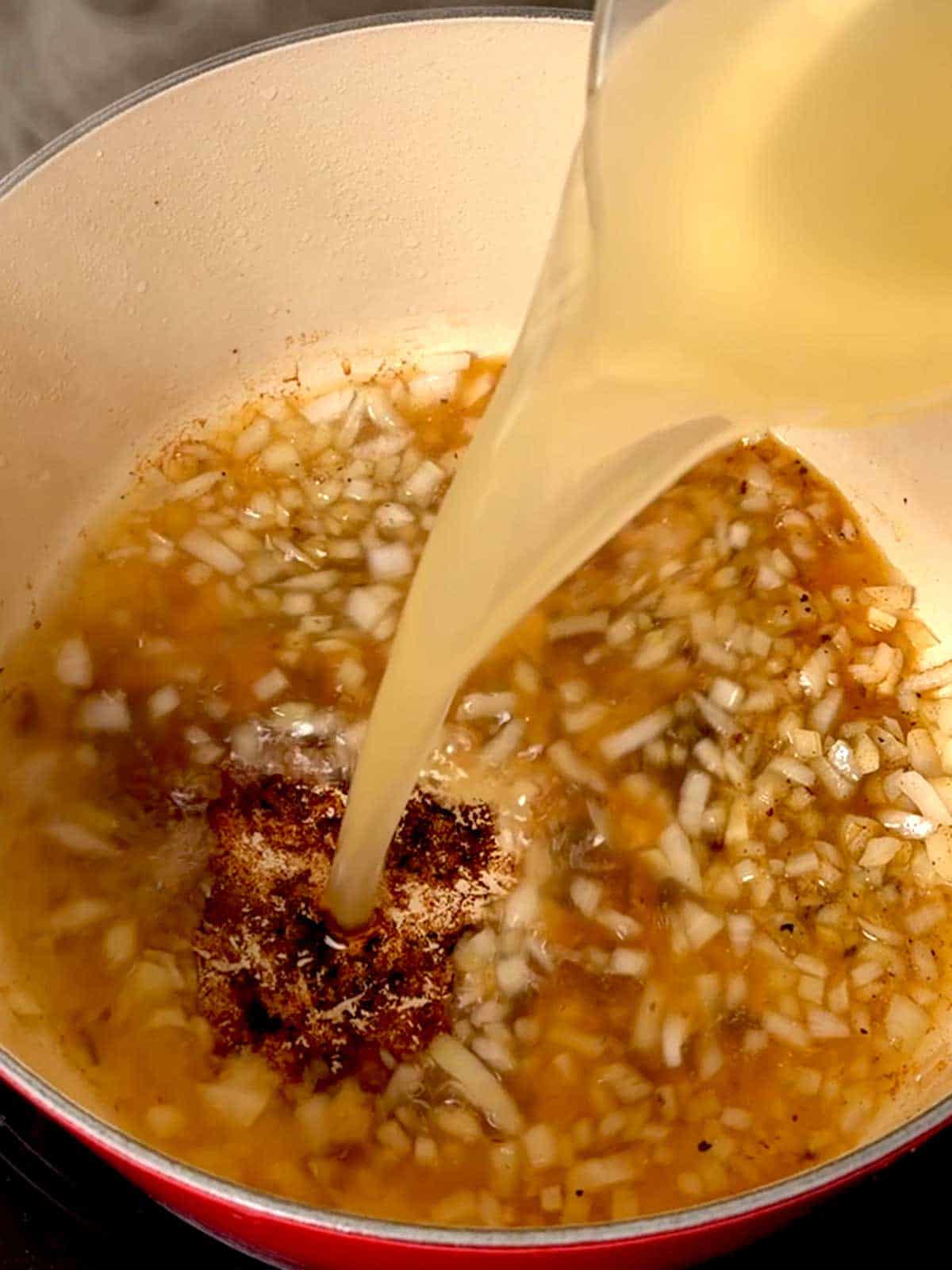 Adding chicken broth to the Dutch oven to deglaze the pan.