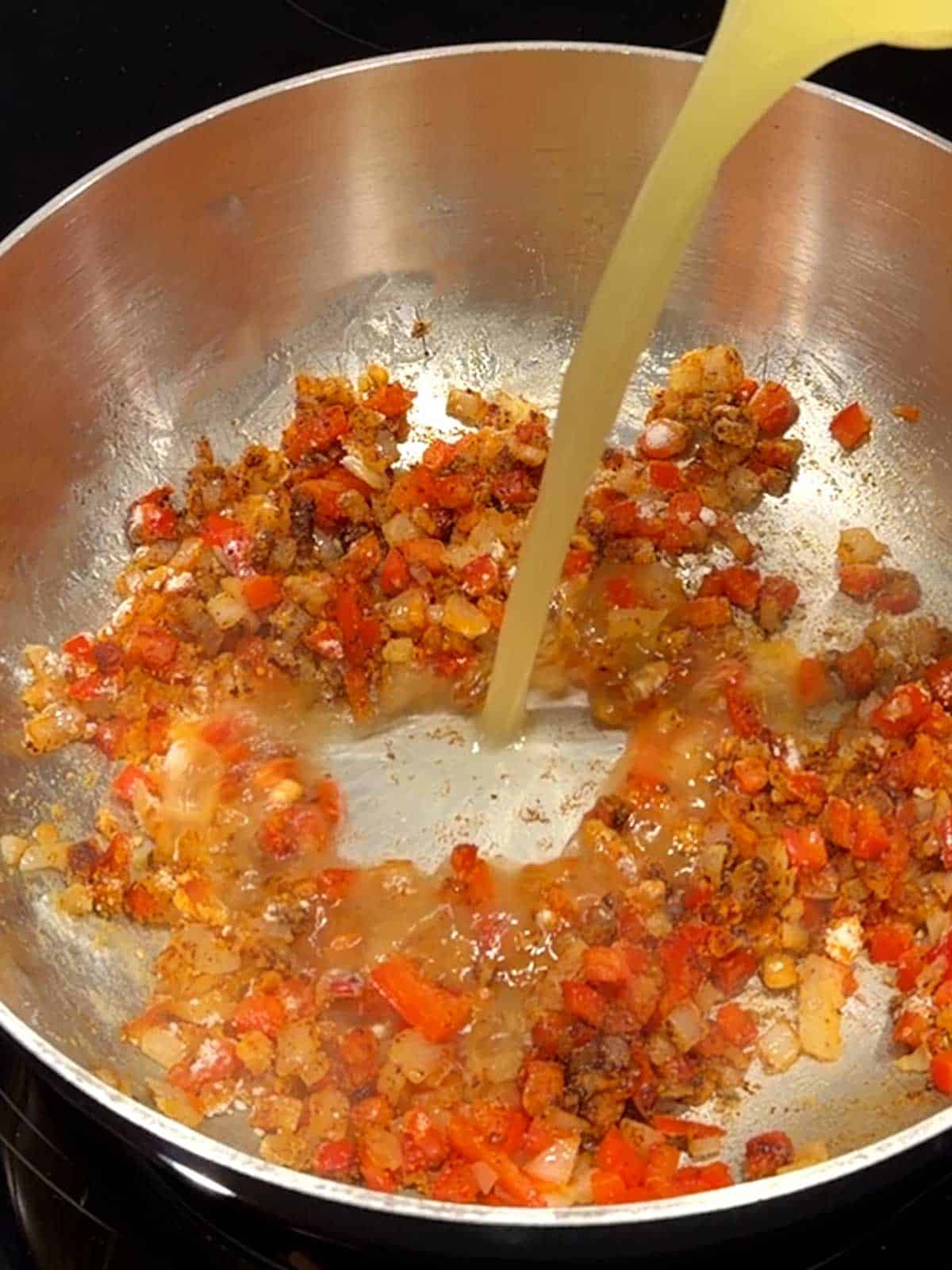 Adding chicken broth to the vwggies coated in flour.