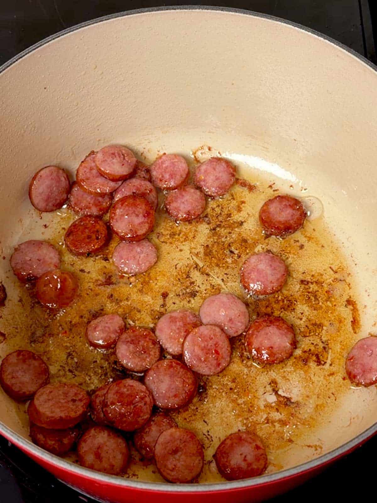 Sliced smoked sausage cooking in a Dutch oven.
