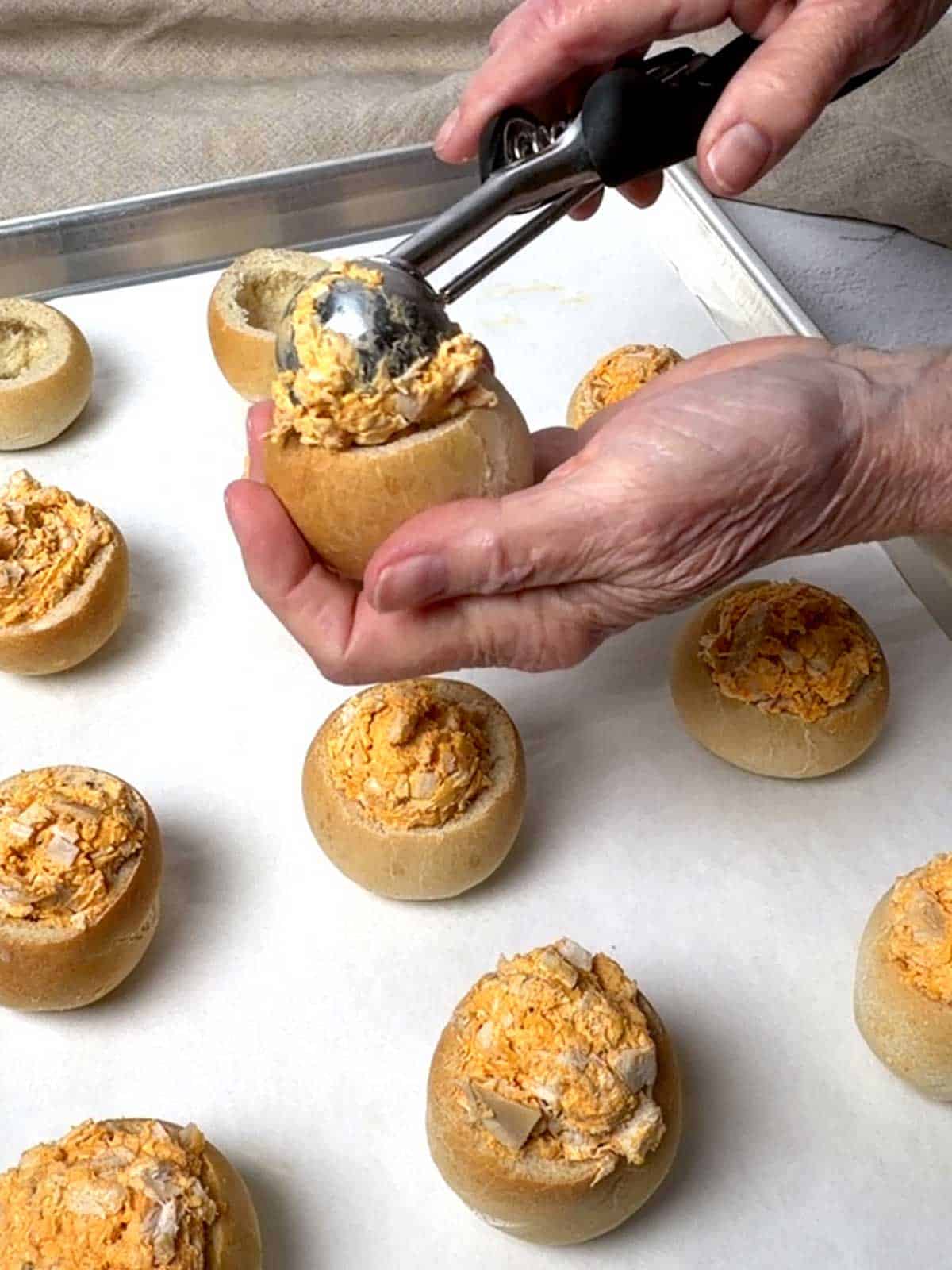 Using an ice cream scoop to add Buffalo chicken filling to mini bread bowls.