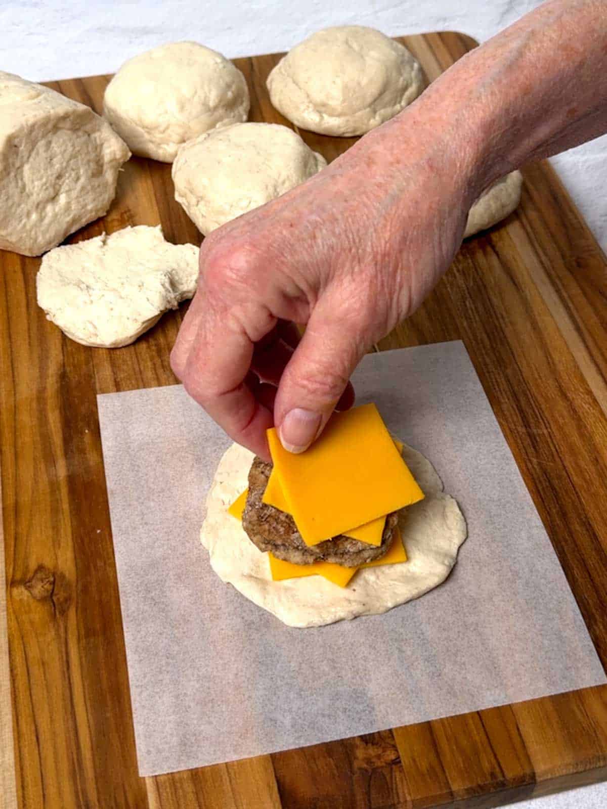 Placing sliced cheese on top of sausage patty.