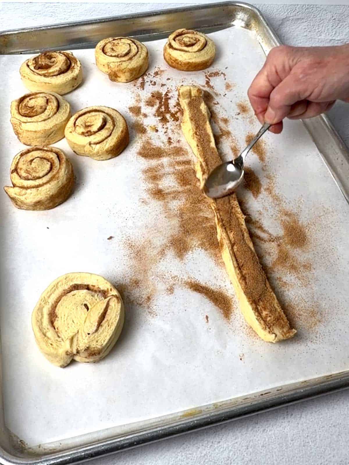 Pressing the cinnamon sugar into the cinnamon roll dough with the back of a small spoon.