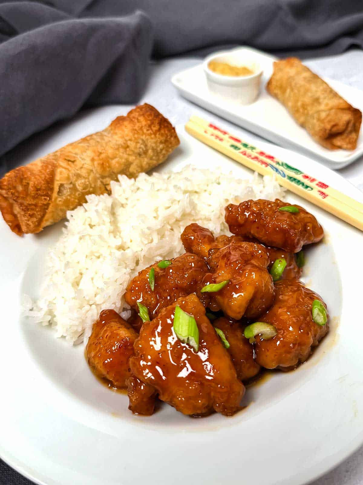 Orange chicken with rice and egg rolls on the side.