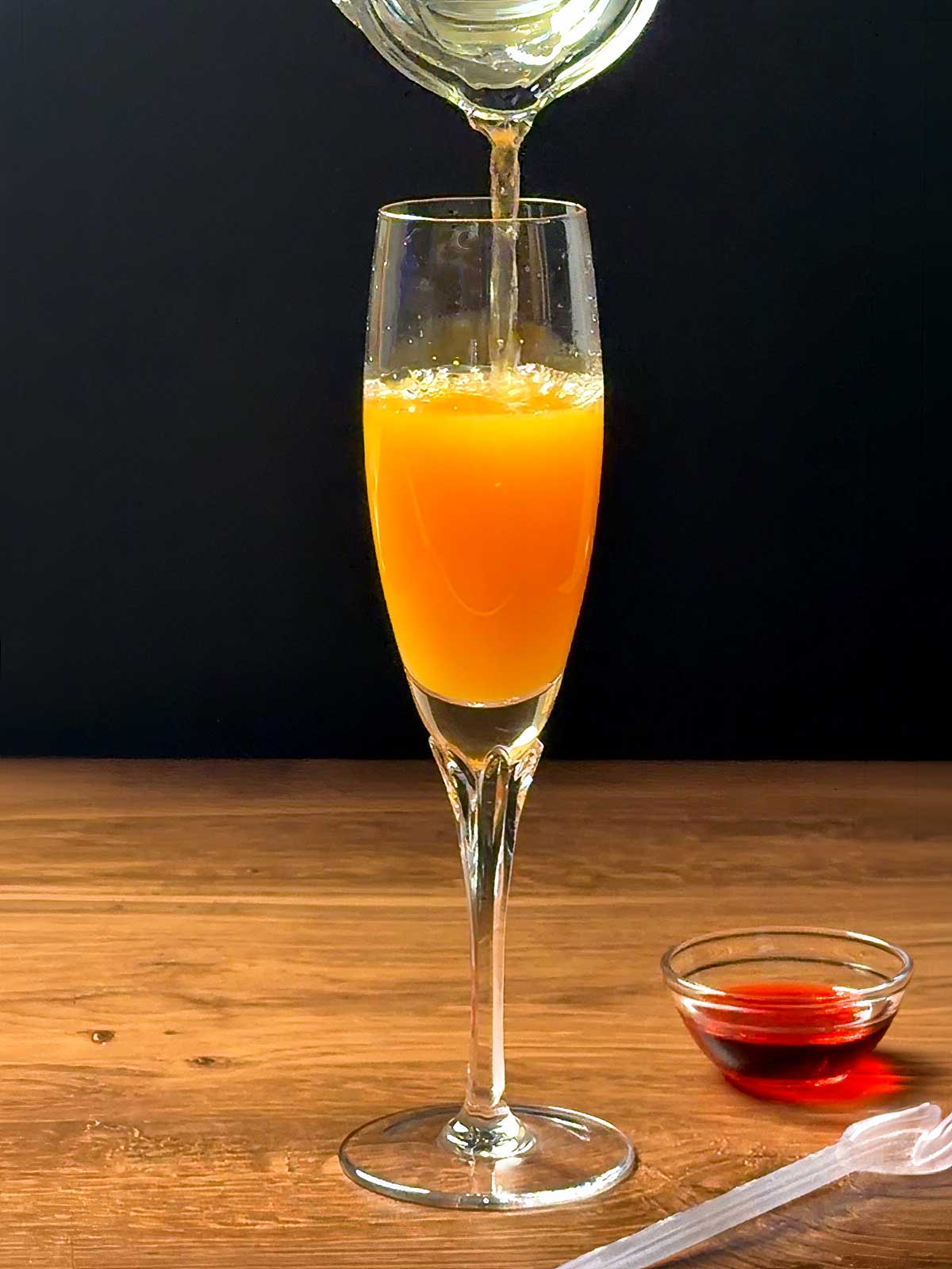Adding sparkling white grape juice to the orange juice in the champagne flute.