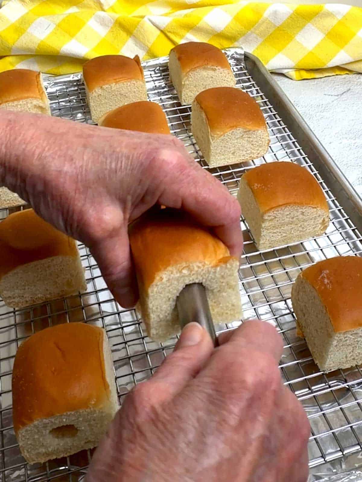 Using a cannoli tube to cut a core into the side of each Hawaiian roll.