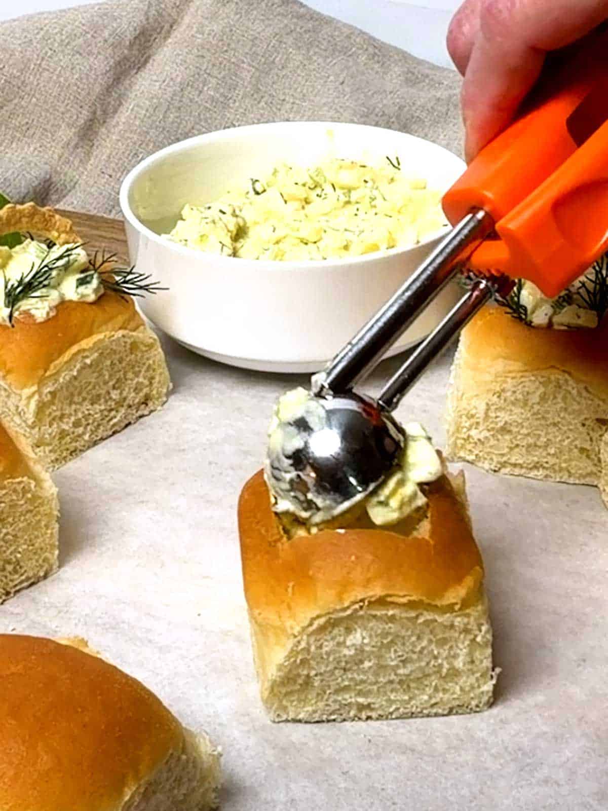 Filling the Hawaiian roll with egg salad using a small scoop.