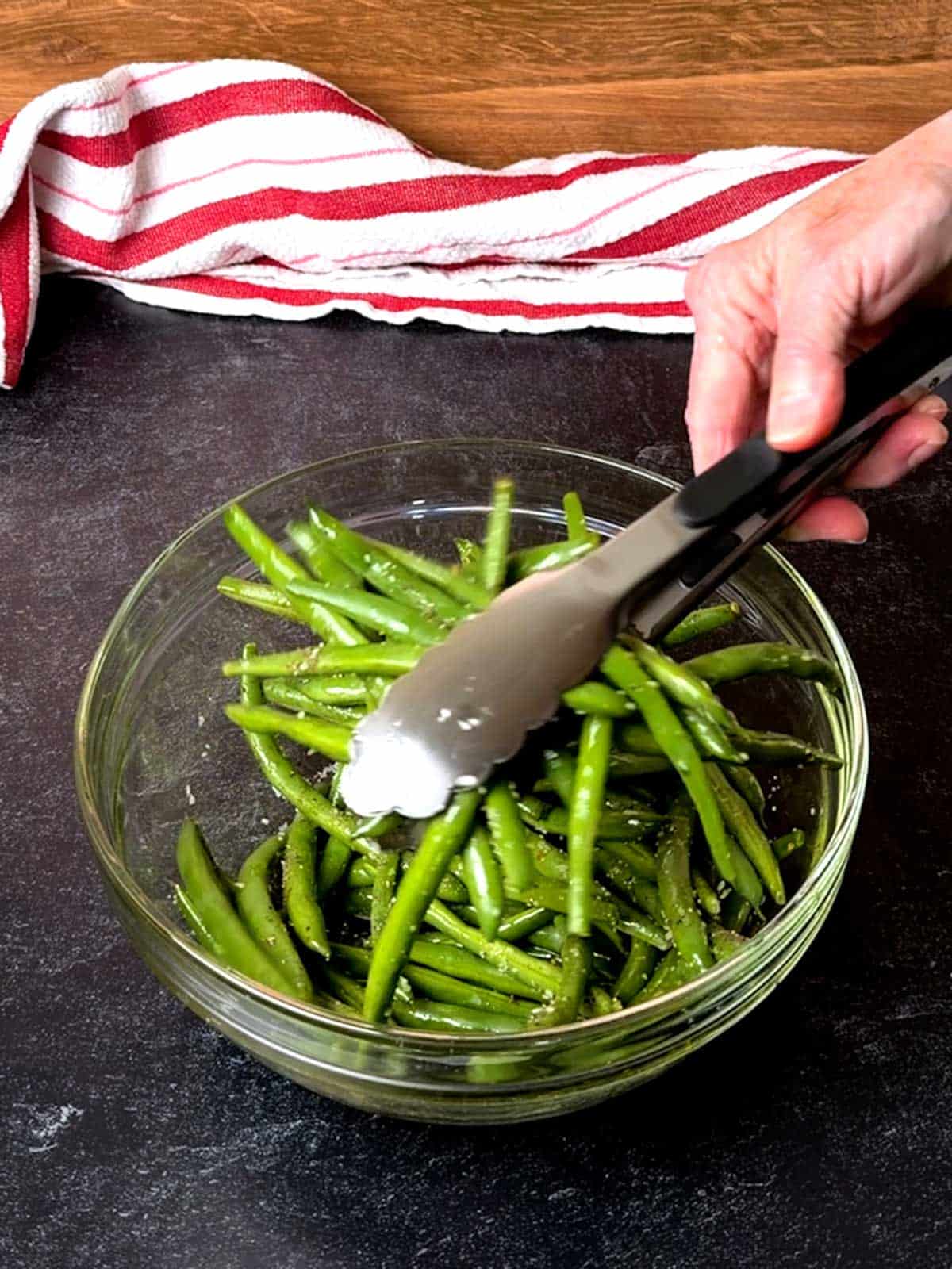 Tossing the green beans with olive oil, salt, and pepper.