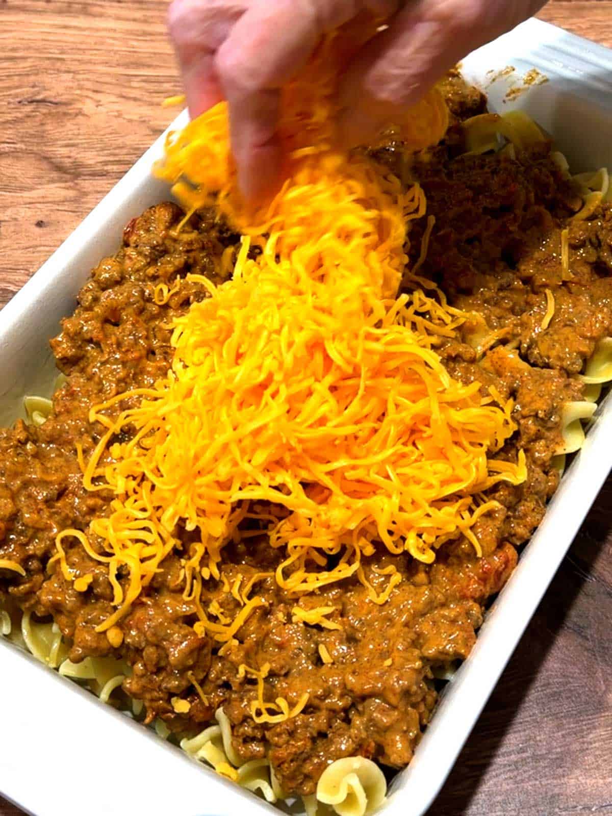 Adding shredded cheddar cheese to the taco noodle casserole.