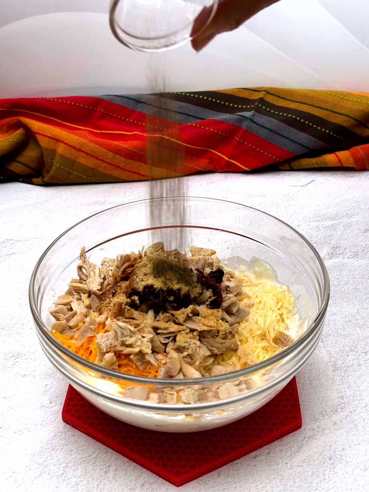 Adding pepper to the other ingredients for the chipotle chicken dip.