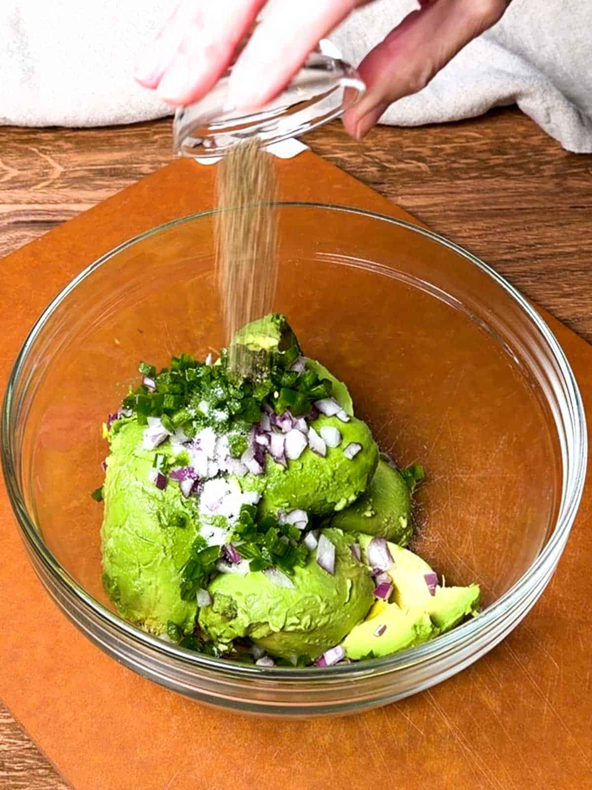 Adding black pepper to the base ingredients for the guacamole.