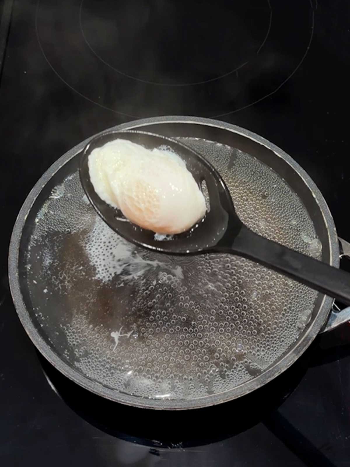 Removing the poached egg with a slotted spoon