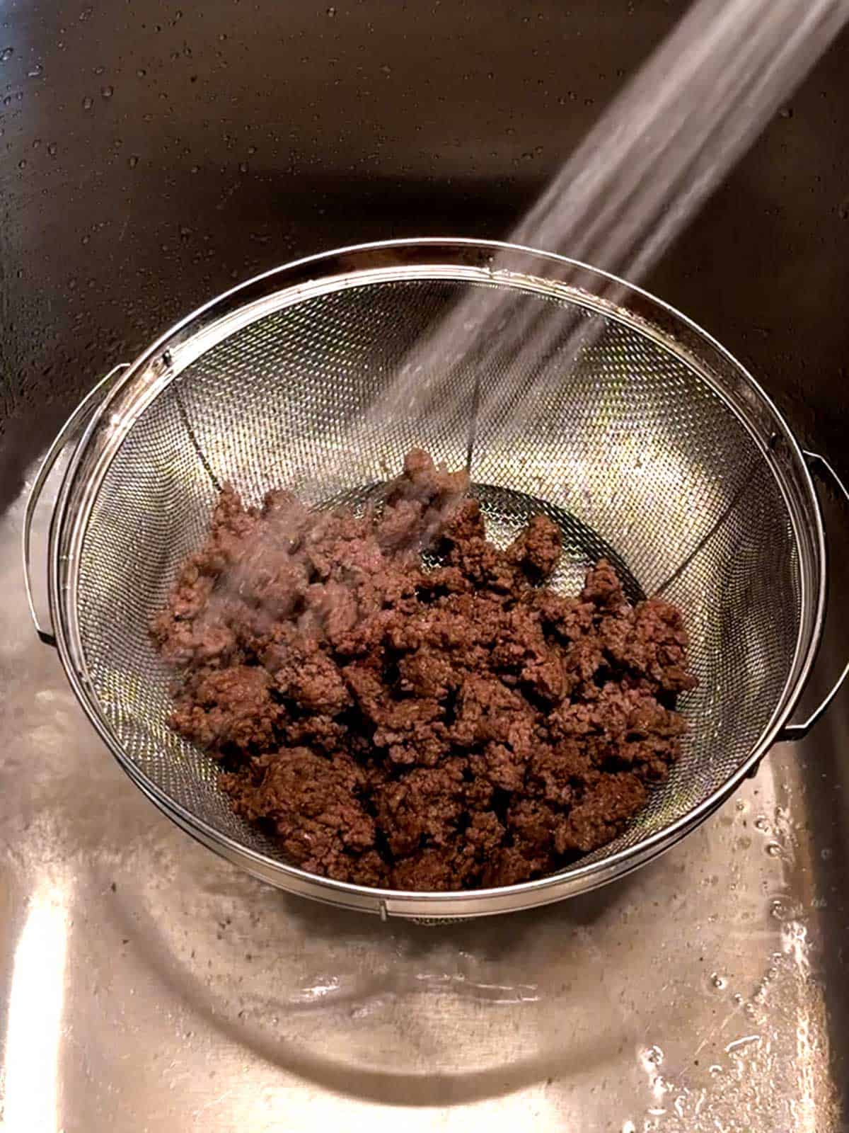 Rinsing the cooked ground beef in a colander.