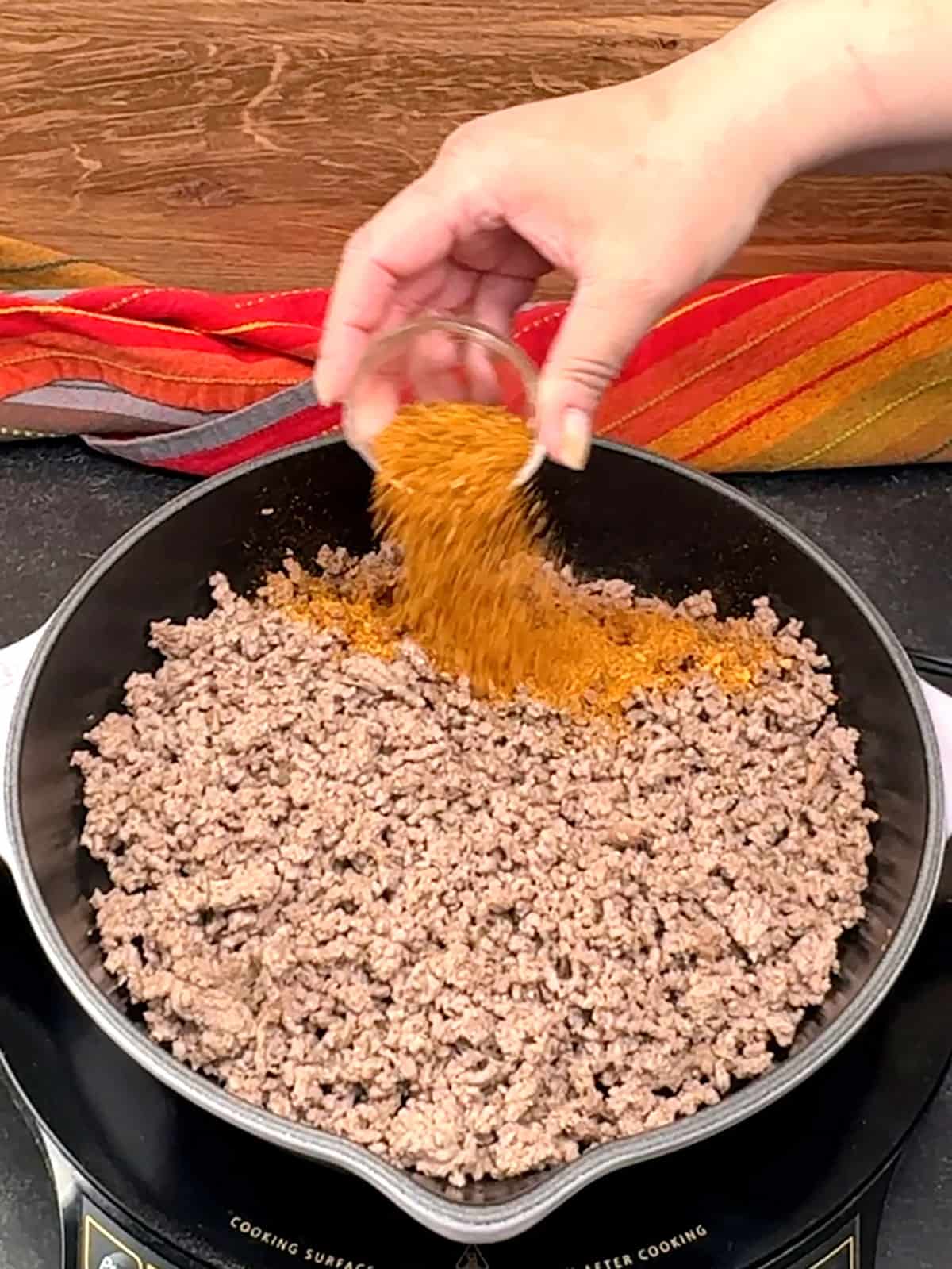 adding taco seasoning to cooked meat