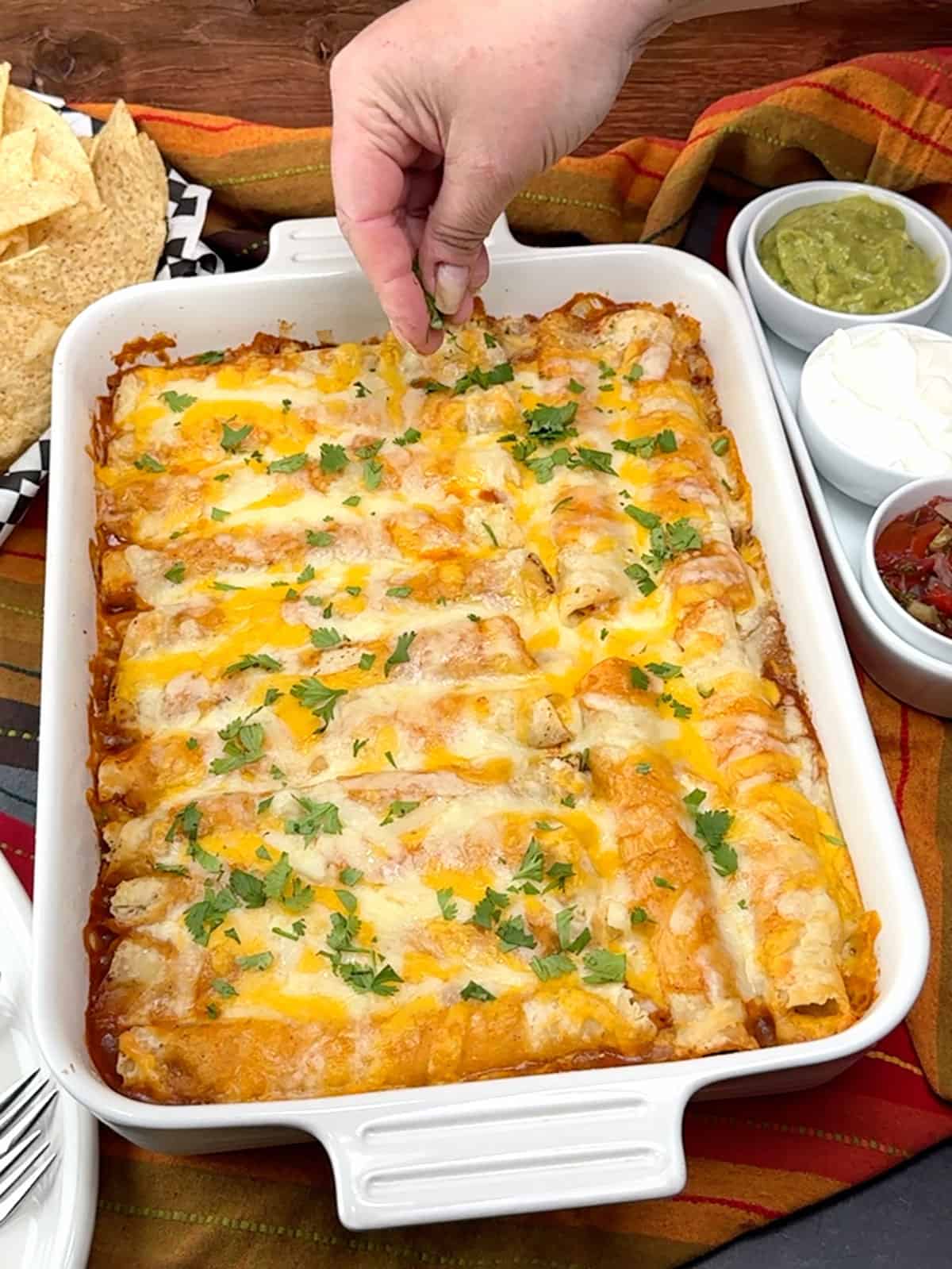 sprinkling cilantro over the top of taquito casserole with beans and rice
