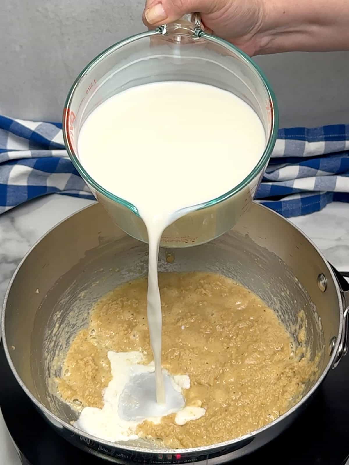 pouring milk into roux to create sauce for Ultimate Baked Macaroni and Cheese with Ham