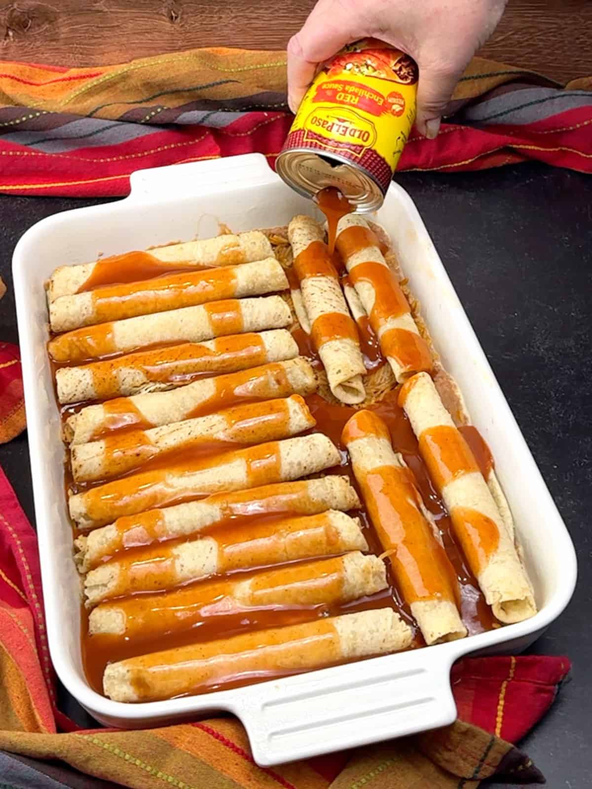 pouring enchilada sauce over taquitos