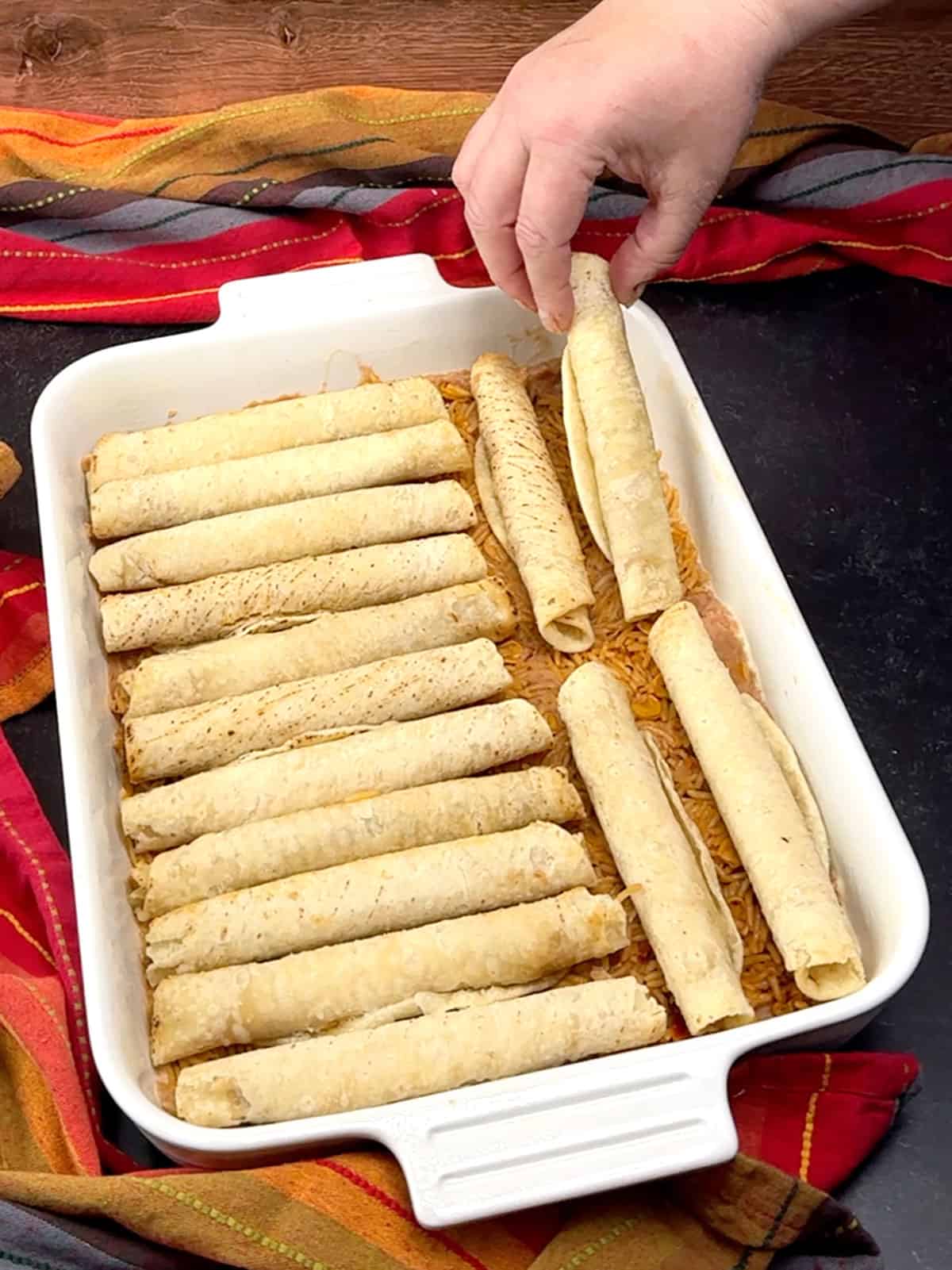 arranging baked taquitos over beans and rice in baking dish