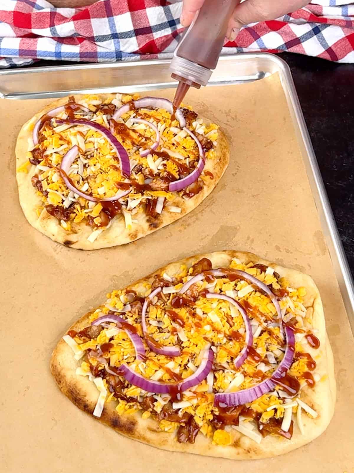 drizzling barbecue sauce over the top of the pizzas