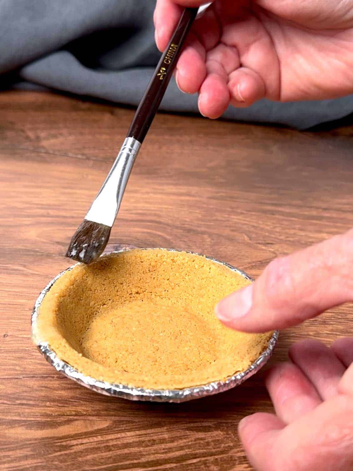 Brushing the rim of the graham cracker crust with melted butter.