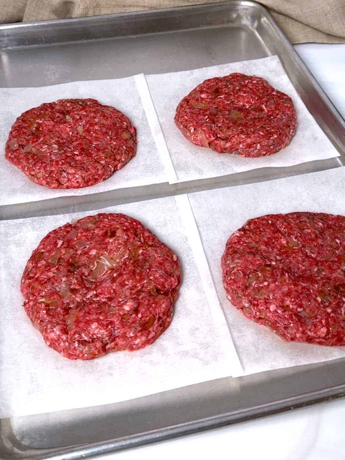 Four hamburger patties on parchment paper.