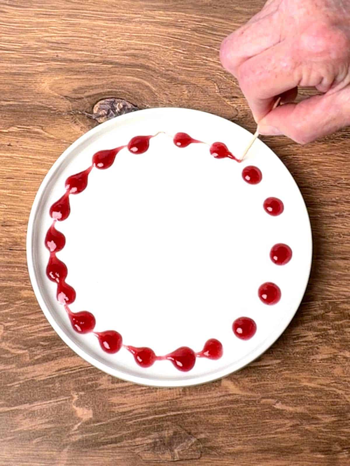 Drawing toothpick through raspberry sauce.