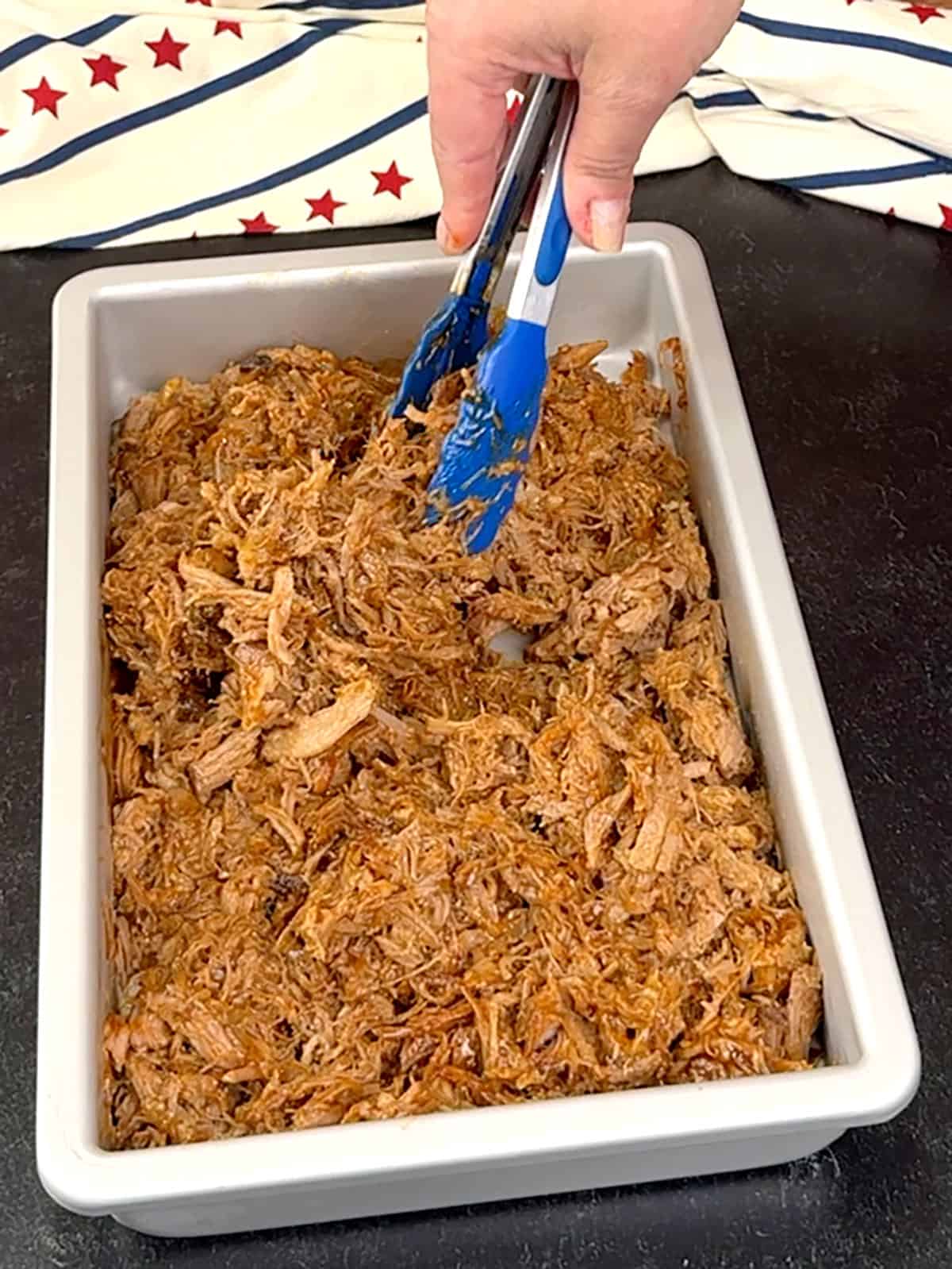mixing pulled pork and sauce with tongs