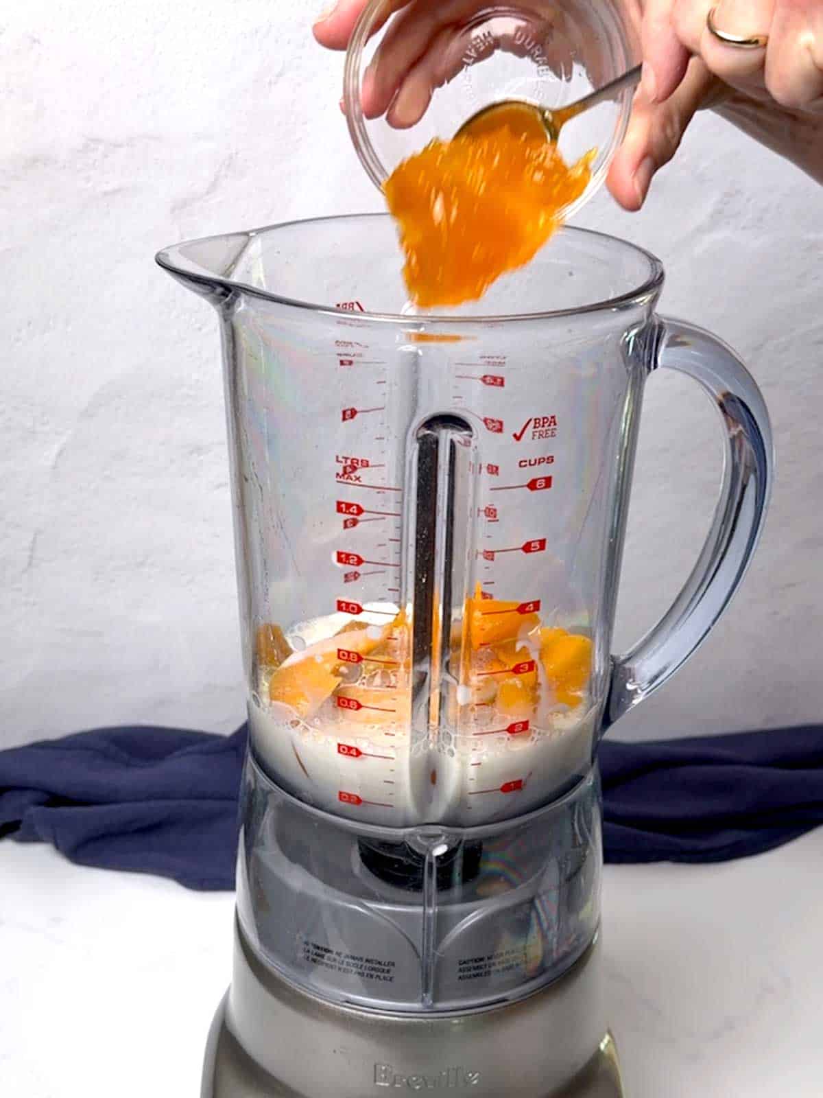 Adding peach spreadable fruit to a blender with the other ingredients.