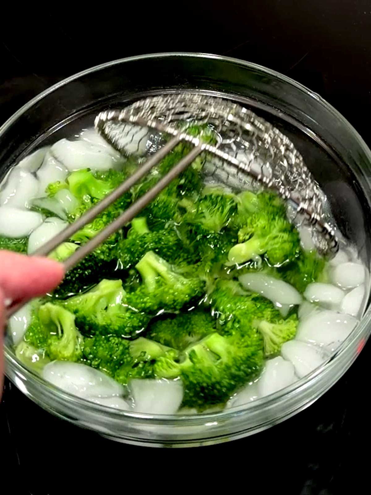 Adding blanched broccoli to ice water bath.