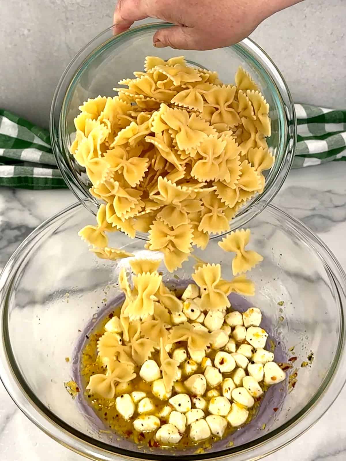 adding pasta to bowl with mozzarella and dressing
