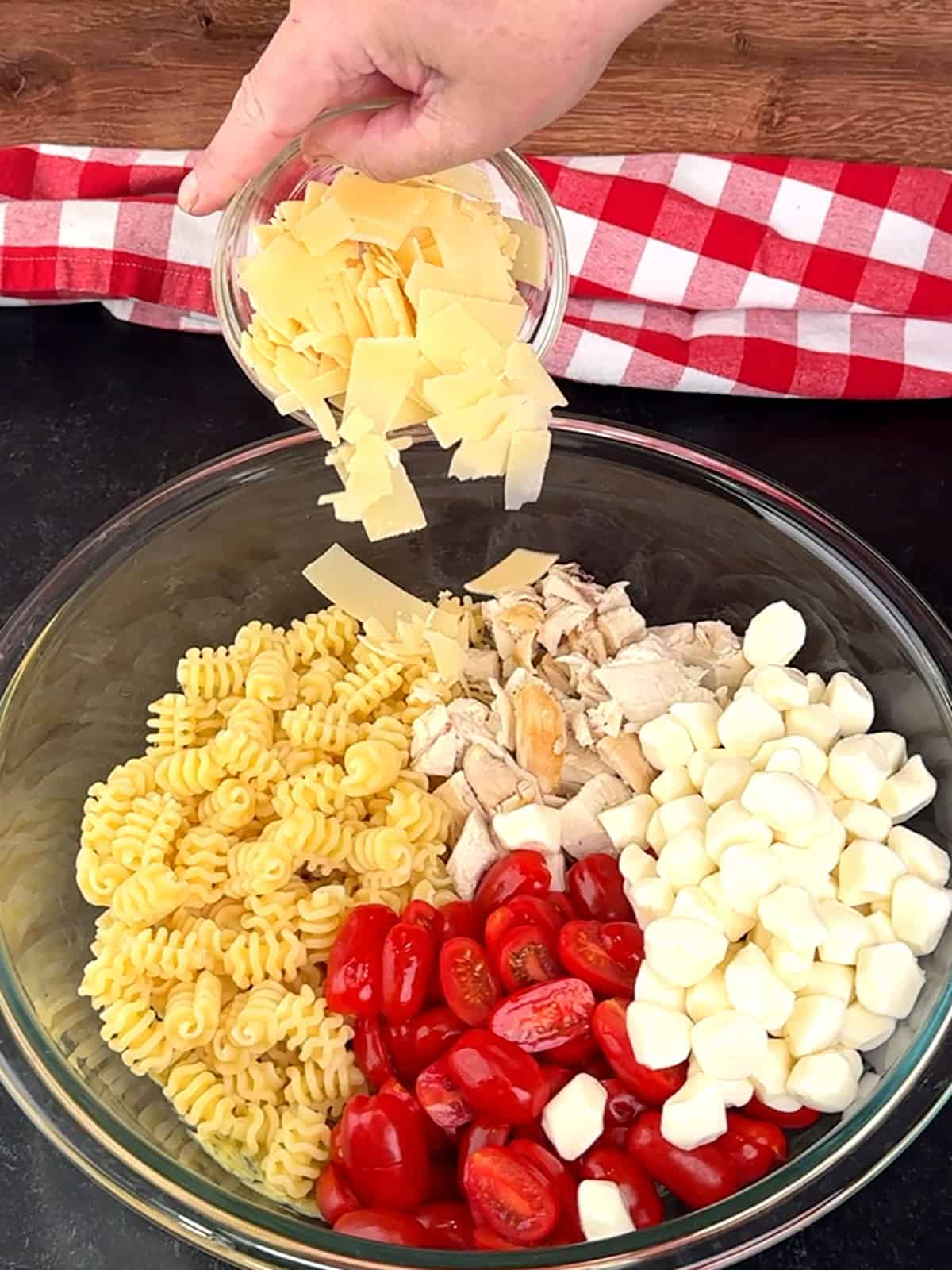 adding pasta, chicken, tomatoes, and cheese to bowl with dressing