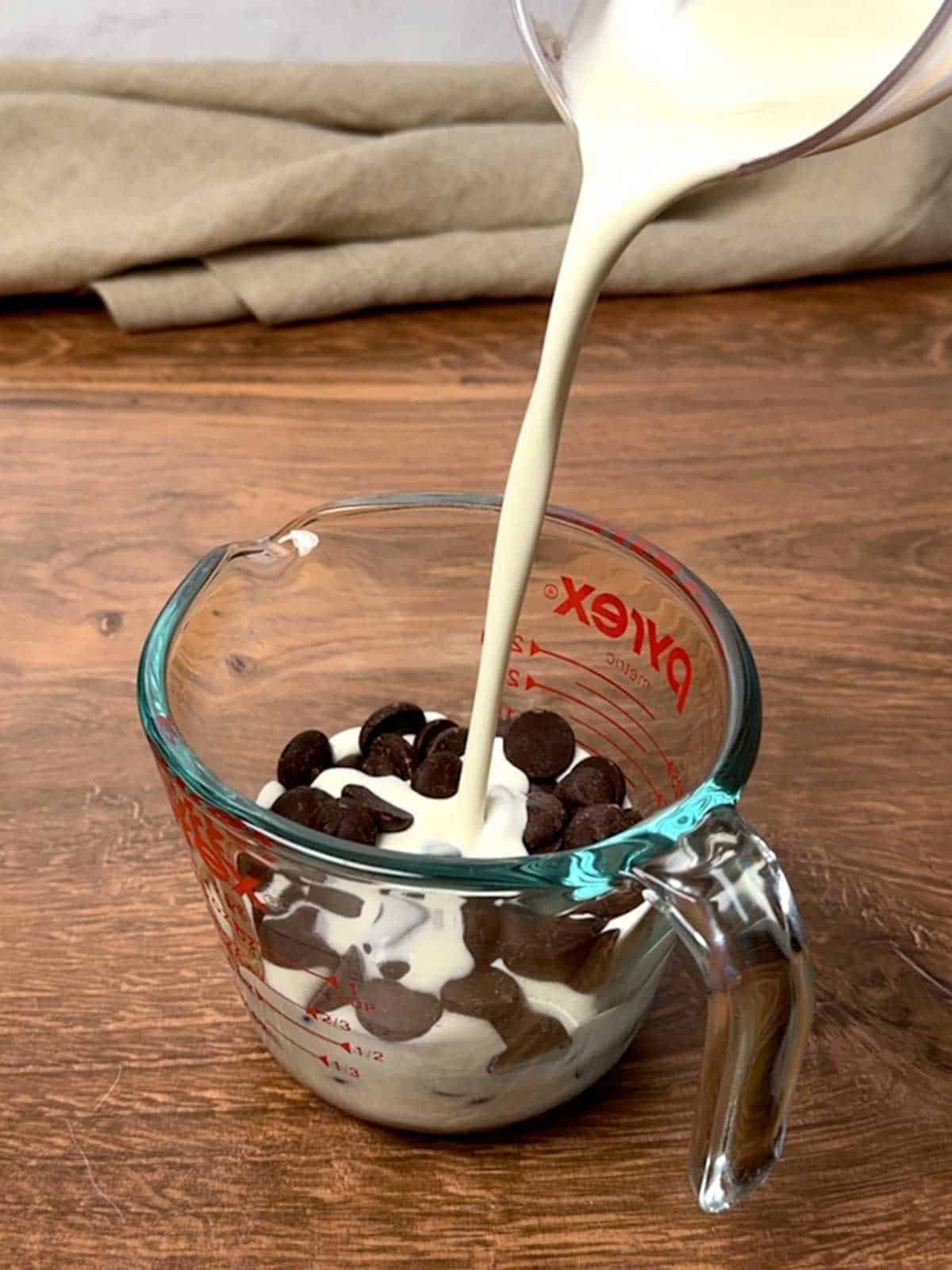 Adding cream to bittersweet chocolate chips in a 1-cup measuring cup.