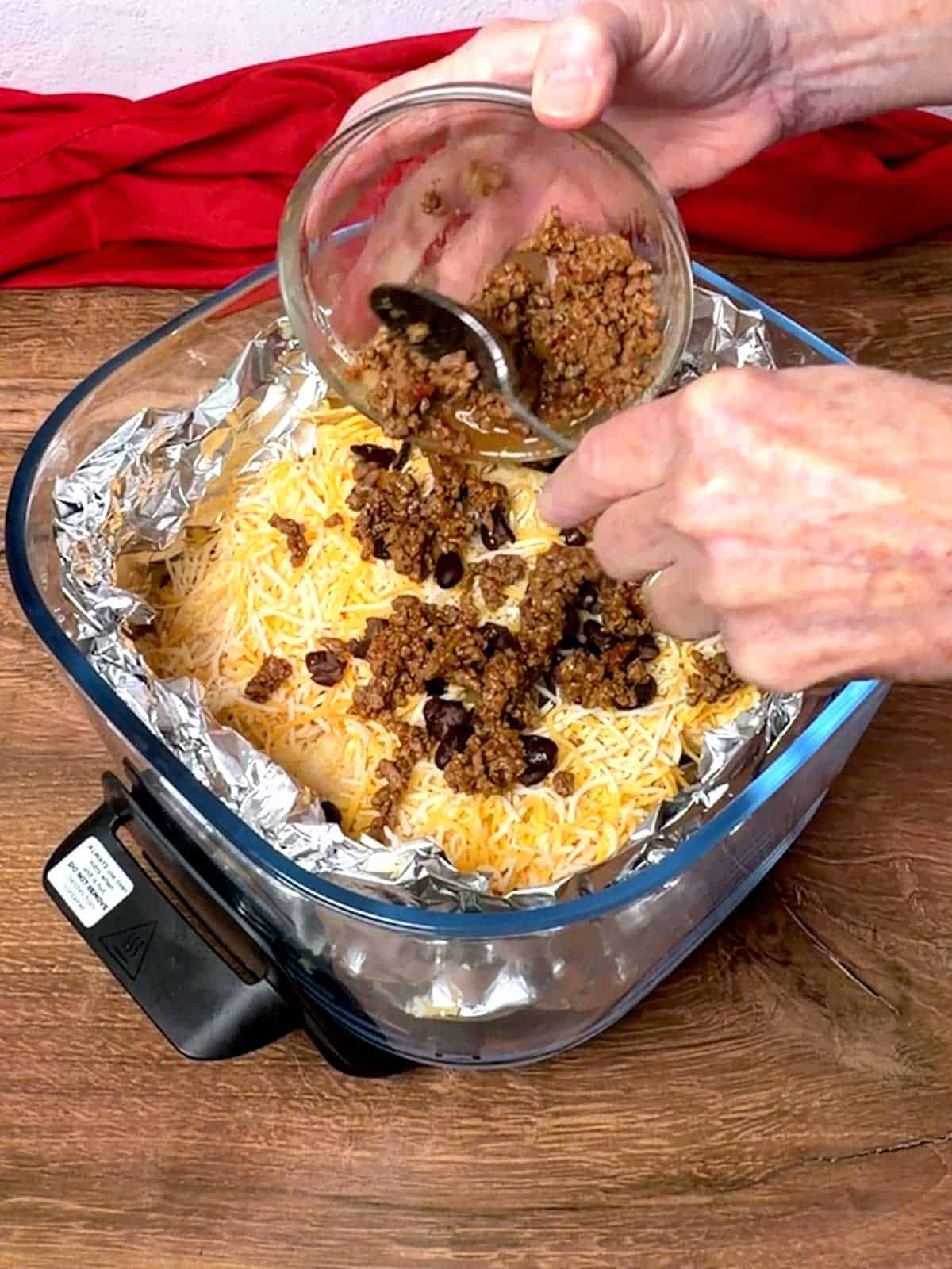 Adding taco meat to the second layer of the nachos.