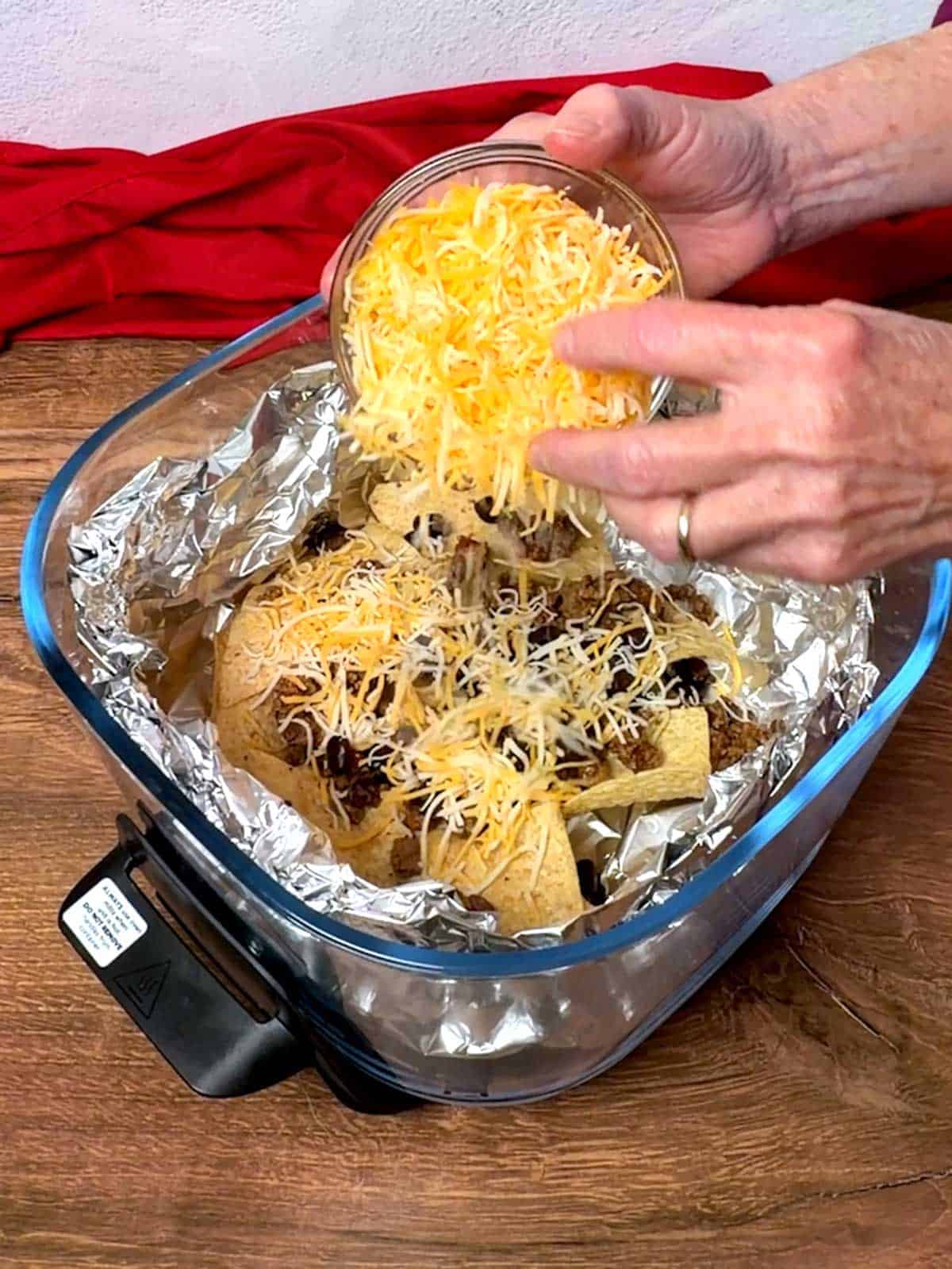 Adding shredded fiesta cheese to the first layer of tortilla chips, taco meat, and black beans.