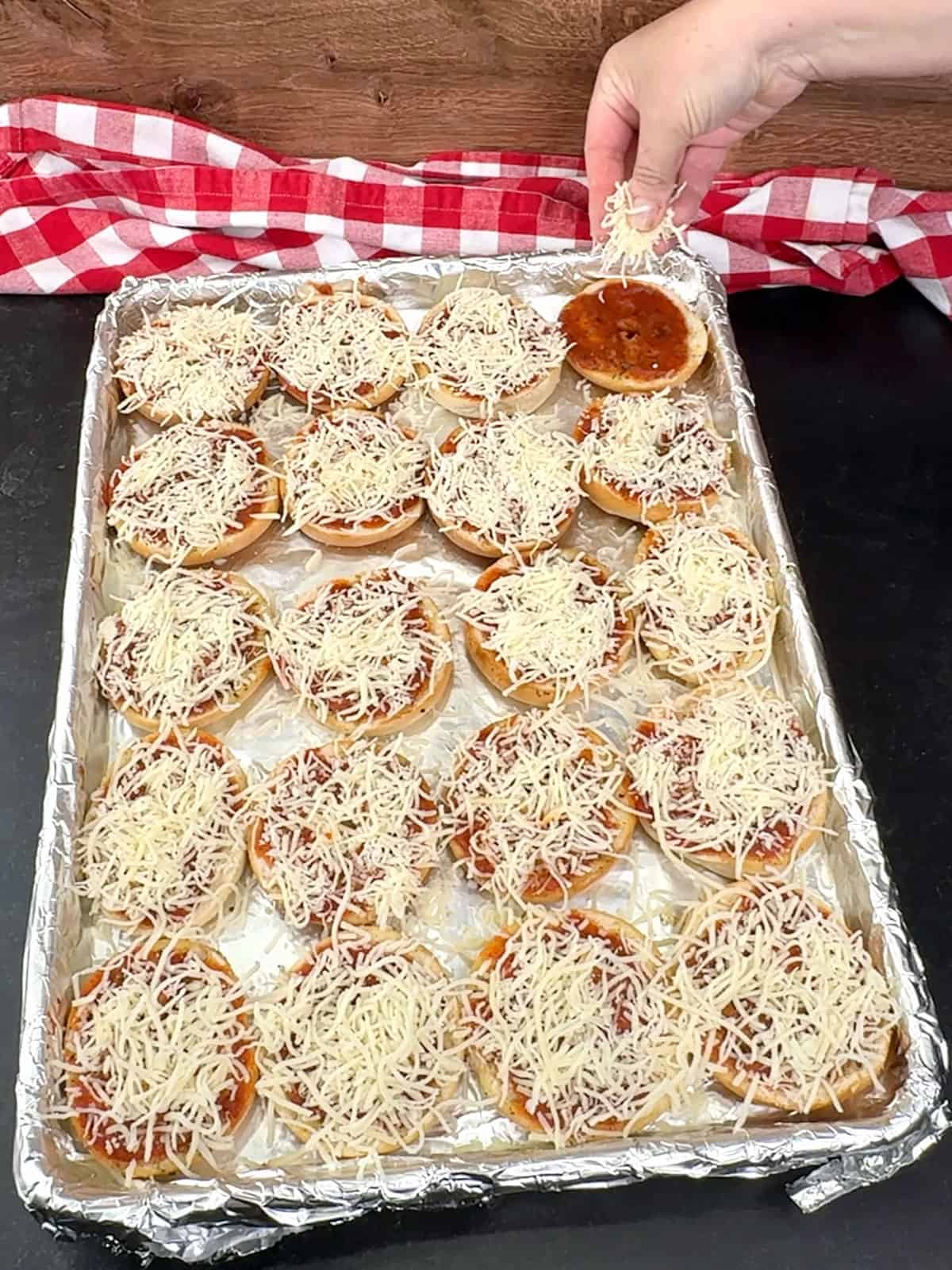 sprinkling cheese over the mini bagels